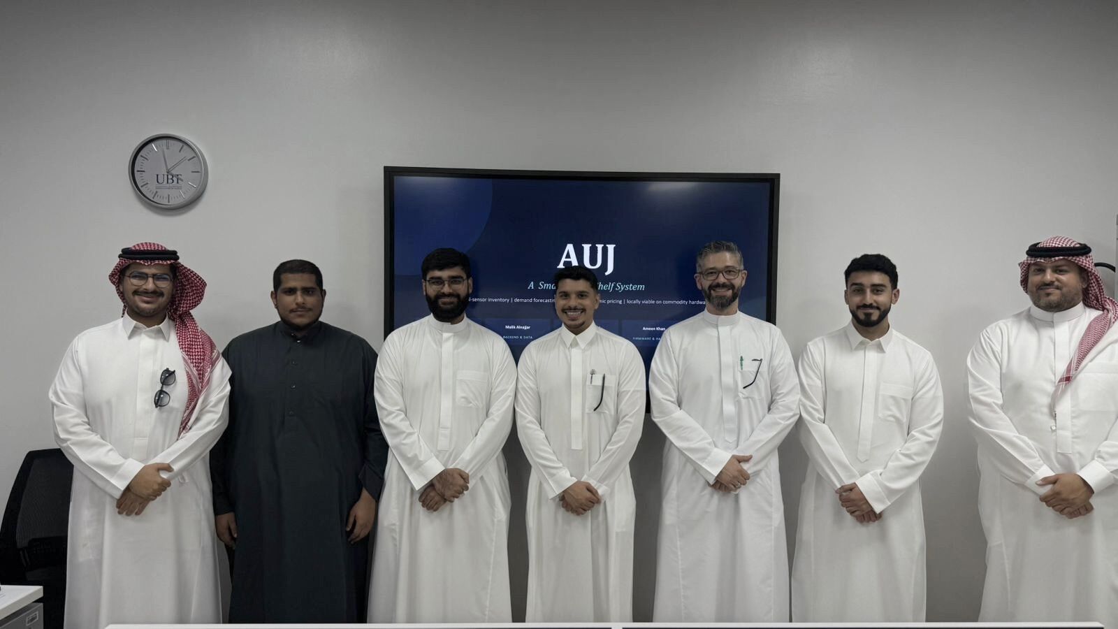 The AUJ capstone team and faculty standing in front of the project presentation screen